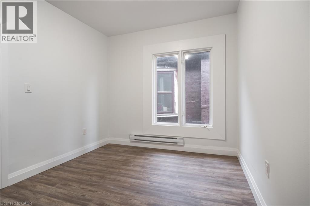Bright room featuring wood-finish flooring, white walls, and a prominent window with white trim - 524 King Street E Unit# 3, Hamilton, ON - Indoor Photo Showing Other Room