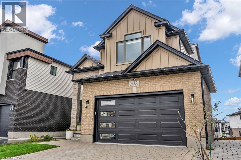 Contemporary exterior featuring a two-car garage with frosted glass inserts, light brick facade, and dark roofline - 2195 Ironwood Road, London, ON - Outdoor