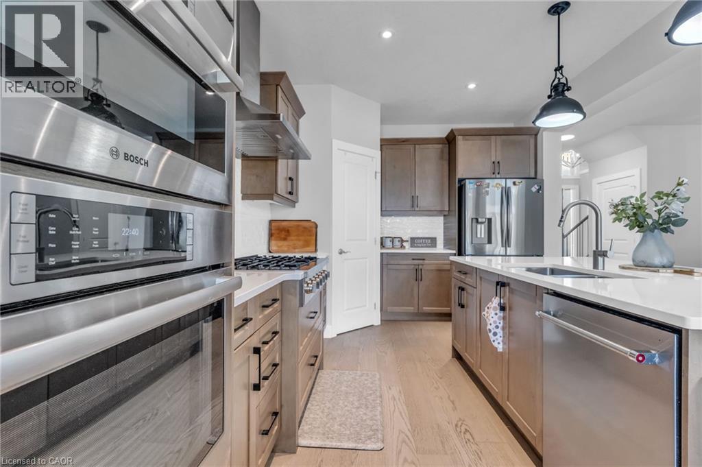 Modern kitchen featuring stainless steel appliances, a center island with sink, pendant lighting, wood-finish flooring, and shaker-style cabinetry - 2195 Ironwood Road, London, ON - Indoor Photo Showing Kitchen With Stainless Steel Kitchen With Upgraded Kitchen