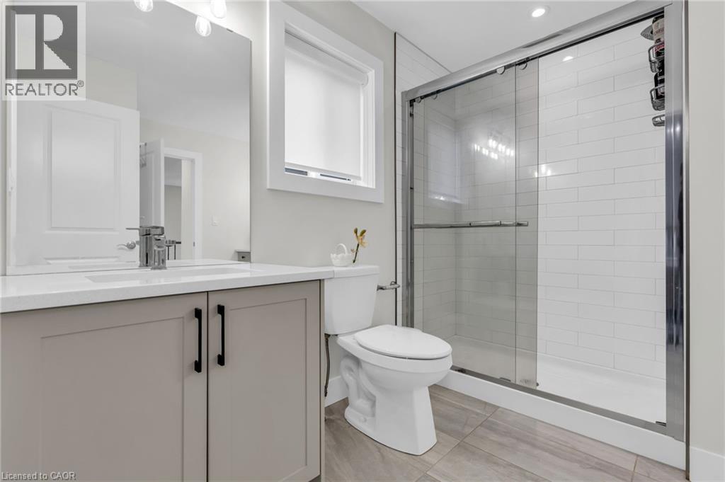 Modern bathroom featuring a glass-enclosed shower with subway tile surround, a single vanity with stone-look countertop, integrated sink, and brushed nickel faucet, and wood-finish tile flooring - 2195 Ironwood Road, London, ON - Indoor Photo Showing Bathroom