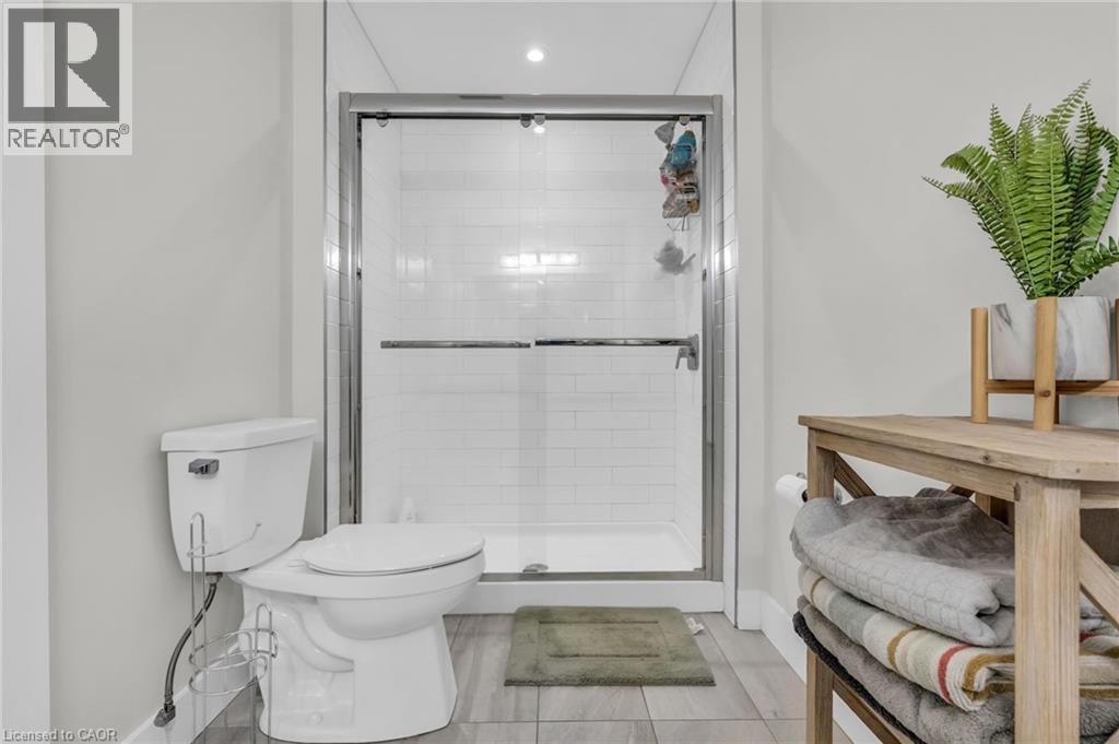 Modern bathroom featuring a glass-enclosed shower with subway tile surround, white toilet, and wood-finish flooring - 2195 Ironwood Road, London, ON - Indoor Photo Showing Bathroom