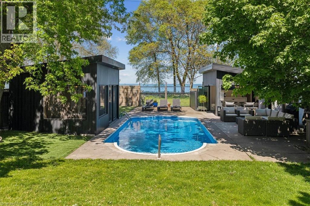 Backyard oasis featuring a swimming pool, concrete patio, and a built-in outdoor kitchen with a covered seating area - 573 Beach Boulevard, Hamilton, ON - Outdoor With In Ground Pool With Backyard
