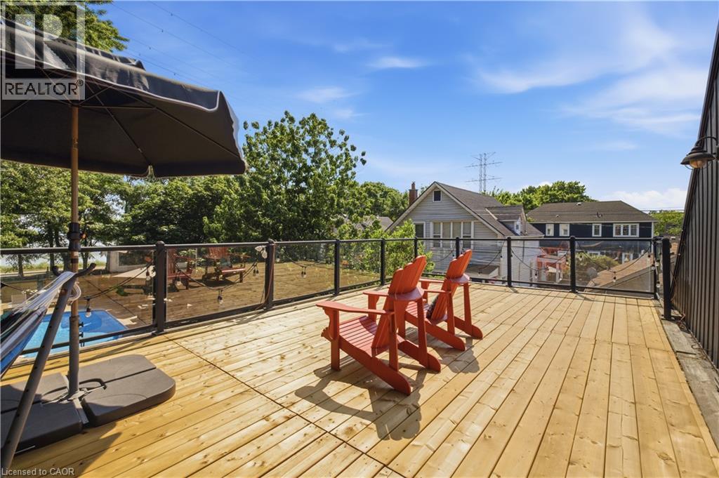 Spacious outdoor deck featuring natural wood planks, a black metal and glass railing, and a side-mounted exterior light fixture - 573 Beach Boulevard, Hamilton, ON - Outdoor With Deck Patio Veranda With Exterior
