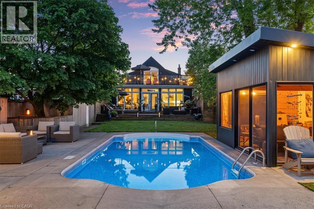 Outdoor living space featuring a swimming pool with concrete surround, an adjacent modern outbuilding with large windows, and a raised patio with a glass railing - 573 Beach Boulevard, Hamilton, ON - Outdoor With In Ground Pool With Deck Patio Veranda