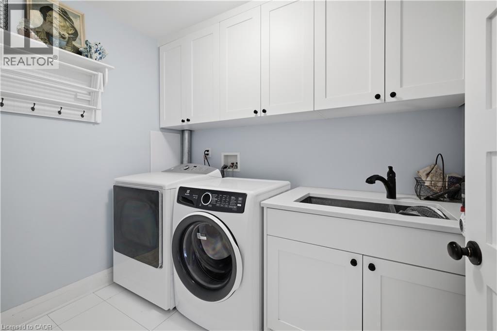 Laundry area featuring white shaker-style cabinetry, a white countertop with an integrated sink, a matte black faucet, and white tile flooring - 573 Beach Boulevard, Hamilton, ON - Indoor Photo Showing Laundry Room