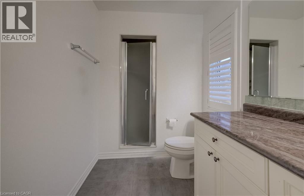 Bathroom featuring a glass-enclosed shower, white toilet, single vanity with a stone countertop, white cabinetry with dark hardware, and gray wood-finish flooring - 52 Pointer Street, Cambridge, ON - Indoor Photo Showing Bathroom
