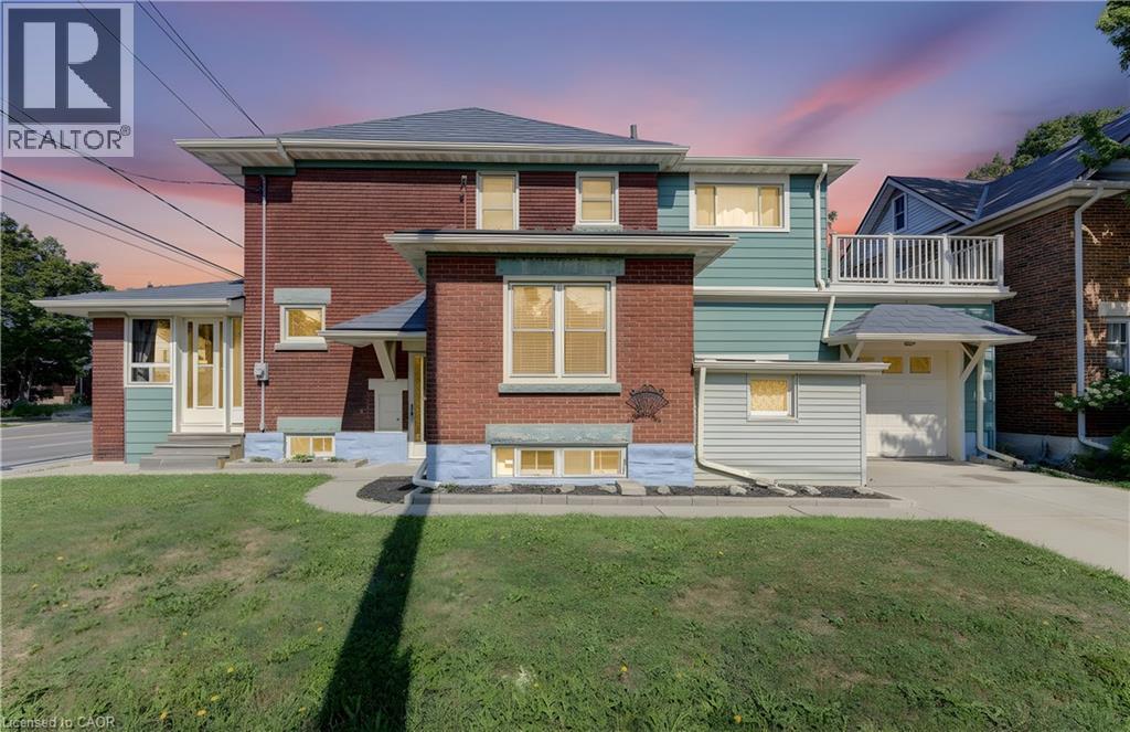 Brick and siding exterior featuring multiple window styles, a prominent front entrance, a garage with an overhead door, an upper-level balcony, and a cement paved driveway - 224 Weber Street E, Kitchener, ON - Outdoor
