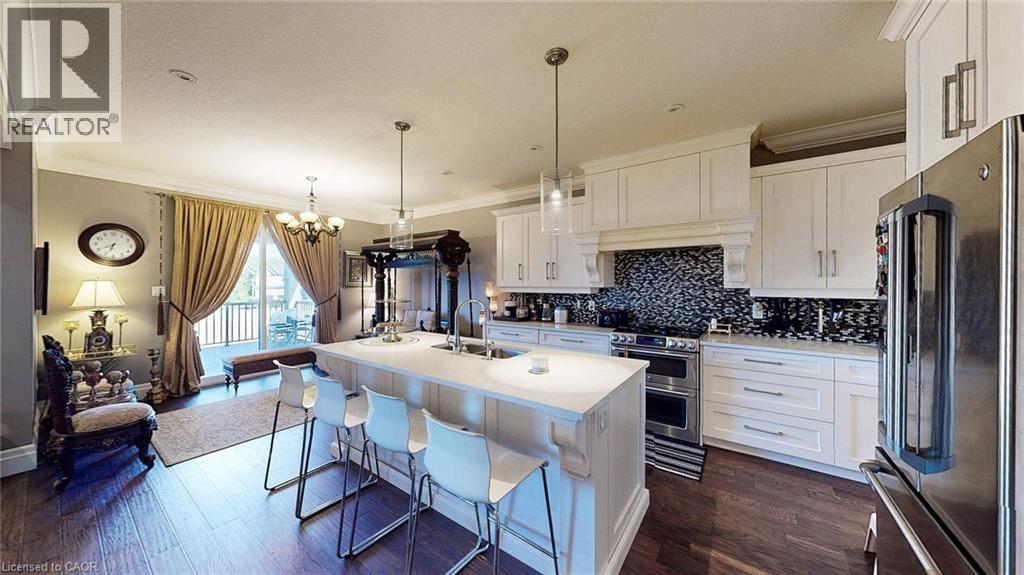 Gourmet kitchen with a large island featuring a breakfast bar, white cabinetry, stainless steel appliances, a mosaic tile backsplash, and wood-finish flooring - 537 Millstream Drive, Waterloo, ON - Indoor Photo Showing Kitchen With Double Sink With Upgraded Kitchen
