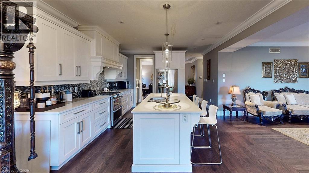 Open-concept kitchen featuring white shaker-style cabinetry, a white countertop island with seating, stainless steel appliances, a multi-tone tile backsplash, and dark wood-finish flooring - 537 Millstream Drive, Waterloo, ON - Indoor Photo Showing Kitchen With Upgraded Kitchen