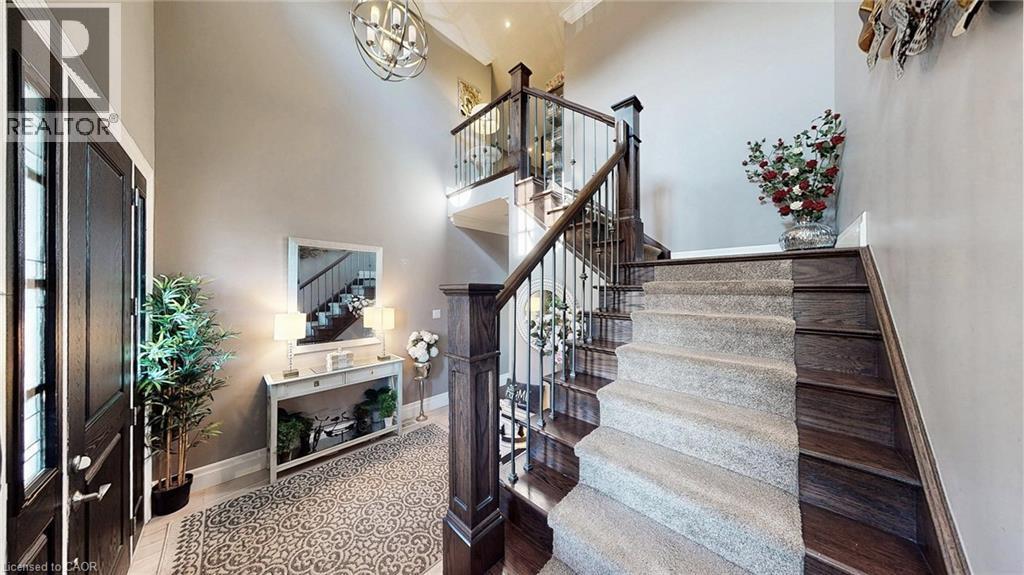 Grand foyer featuring a dark wood front door with sidelights, a double-height ceiling, and a prominent staircase with dark wood treads, light-toned carpet runner, and wrought iron balusters - 537 Millstream Drive, Waterloo, ON - Indoor Photo Showing Other Room