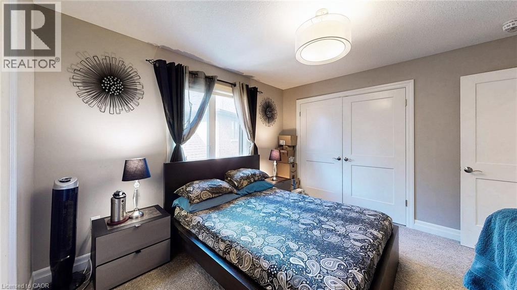 Bright bedroom featuring light gray walls, plush carpet flooring, a multi-panel window with curtains, a built-in double-door closet, and a contemporary ceiling light fixture - 537 Millstream Drive, Waterloo, ON - Indoor Photo Showing Bedroom
