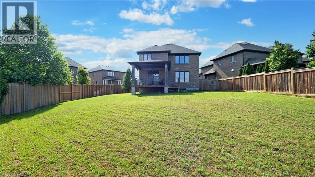 Expansive rear yard featuring a large grass area, wood privacy fencing, and mature perimeter trees - 537 Millstream Drive, Waterloo, ON - Outdoor With Backyard
