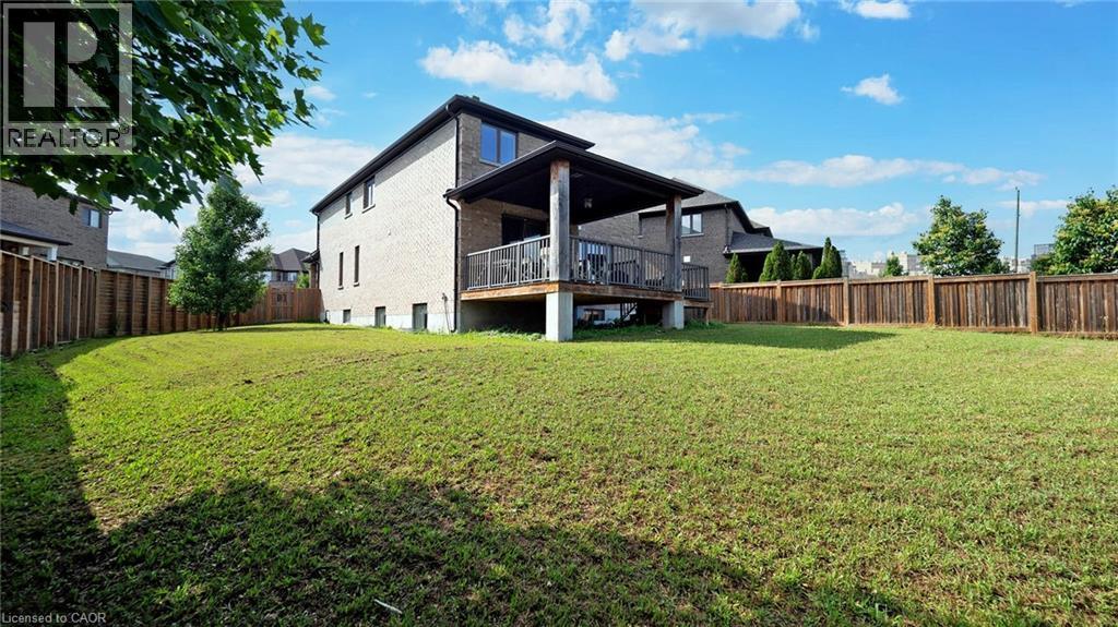 Expansive backyard featuring a manicured lawn, full privacy fencing, and a raised wooden deck with a covered patio - 537 Millstream Drive, Waterloo, ON - Outdoor With Deck Patio Veranda