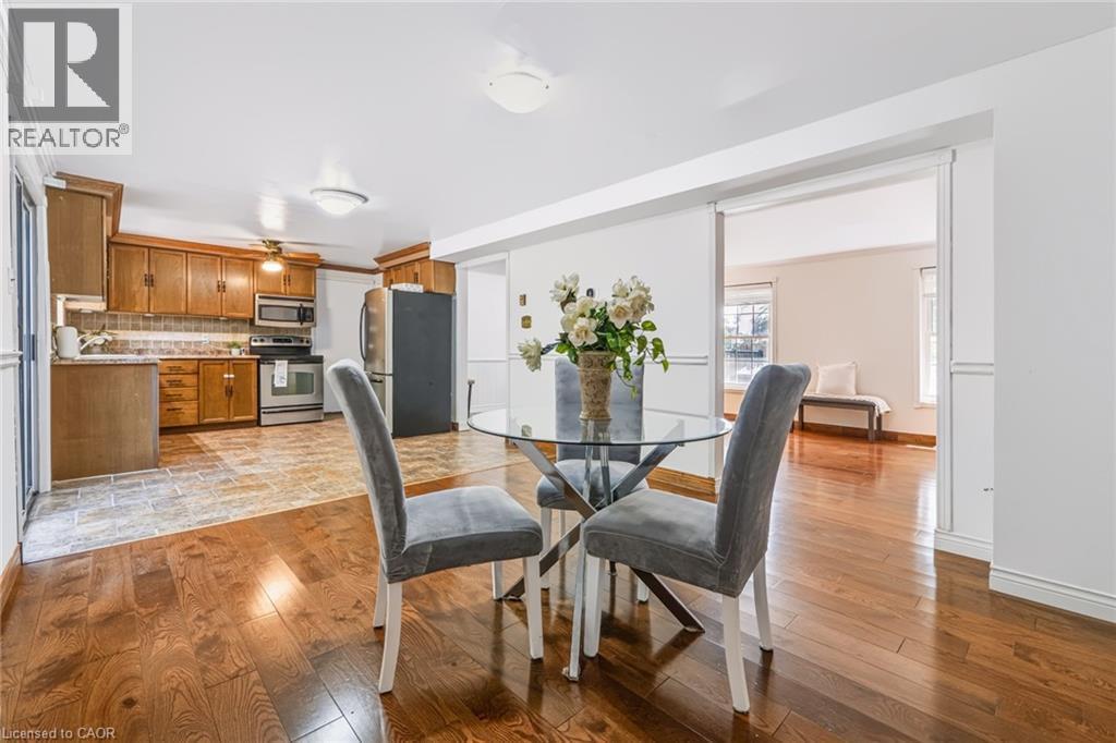Open-concept dining area featuring wood-finish flooring, a kitchen with wood cabinetry, stainless steel appliances, and a tile backsplash, with a separate living space beyond - 34 Peachtree Crescent, Cambridge, ON - Indoor Photo Showing Dining Room