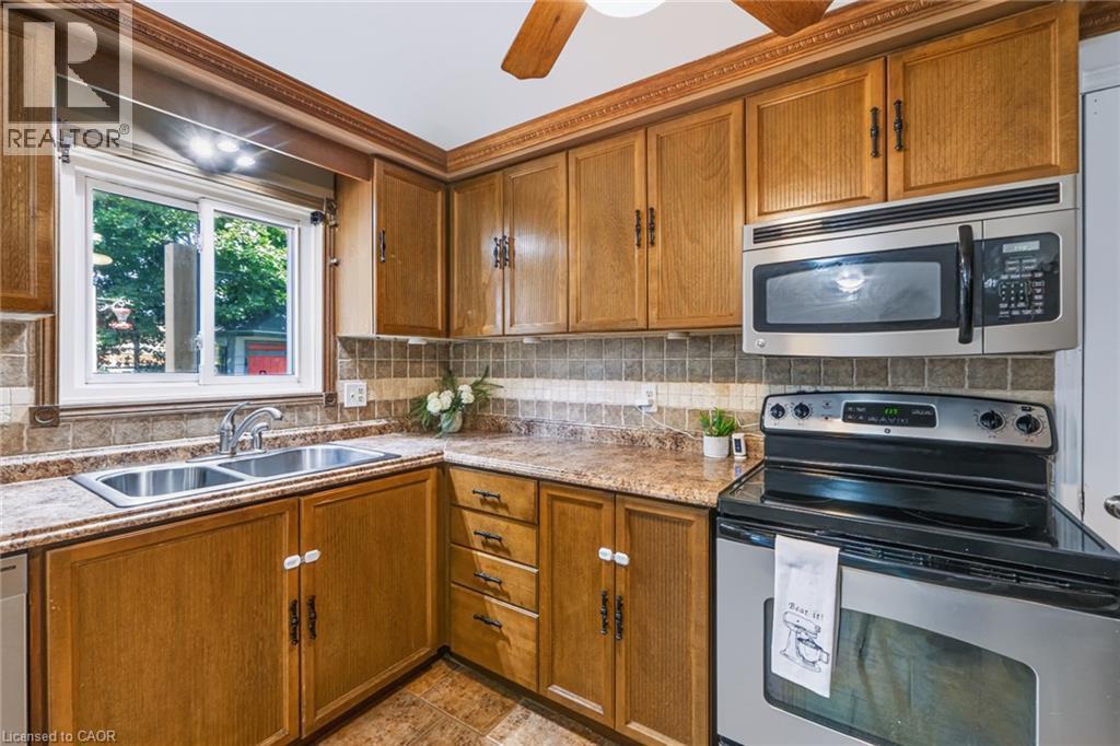 Kitchen featuring wood-finish cabinetry, stainless steel appliances, a double basin sink, and a tiled backsplash - 34 Peachtree Crescent, Cambridge, ON - Indoor Photo Showing Kitchen With Double Sink