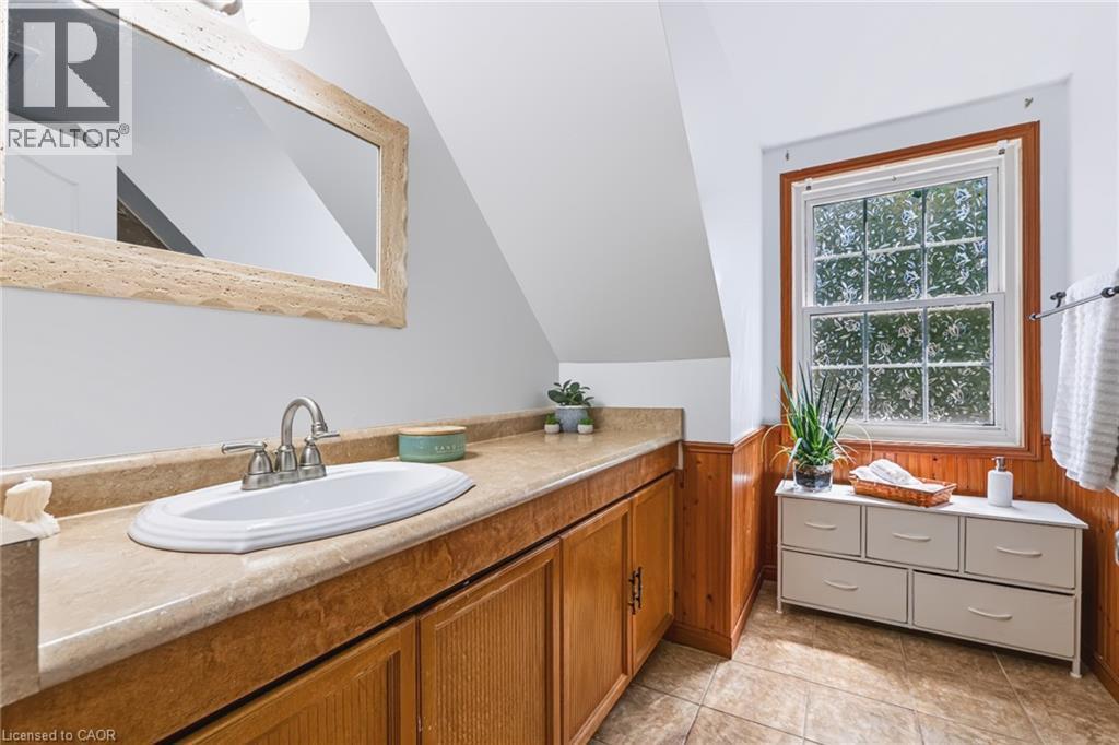 Bathroom featuring a wood vanity with an integrated sink, a rectangular mirror with a textured frame, and a window with wood trim - 34 Peachtree Crescent, Cambridge, ON - Indoor Photo Showing Bathroom