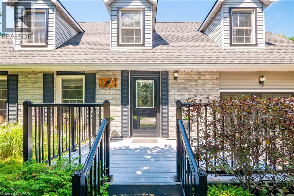 Front exterior featuring light-toned brick, dormer windows, and a black paneled entry door with decorative glass - 34 Peachtree Crescent, Cambridge, ON - Outdoor With Deck Patio Veranda