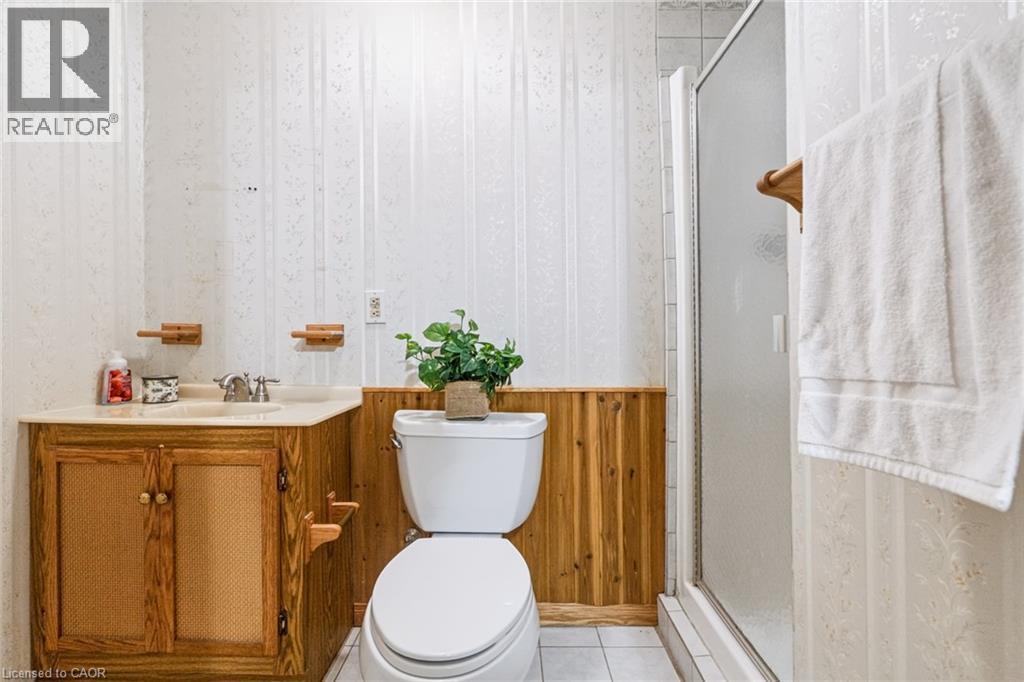 Bathroom featuring a wood-finish vanity with an integrated sink and light-toned countertop, wainscoting, and a shower enclosure with a frosted glass panel - 34 Peachtree Crescent, Cambridge, ON - Indoor Photo Showing Bathroom