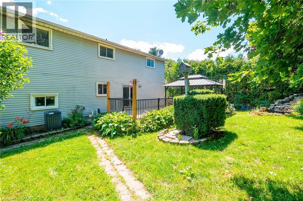 Rear exterior featuring light-colored siding, multiple windows, and a ground-level deck with black railings - 34 Peachtree Crescent, Cambridge, ON - Outdoor