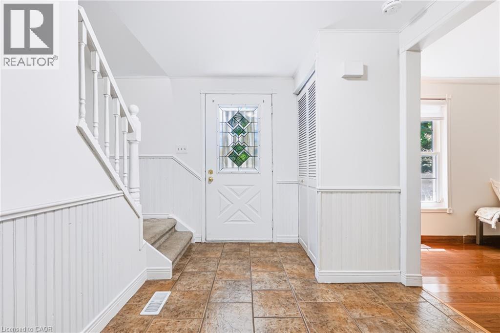 Foyer featuring tile flooring, white wainscoting, a staircase with carpeting on treads, a front door with decorative glass inserts, and louvered closet doors - 34 Peachtree Crescent, Cambridge, ON - Indoor Photo Showing Other Room
