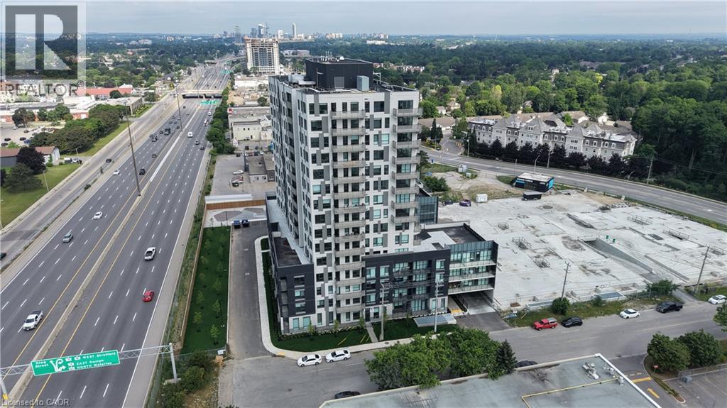 Modern high-rise residential building featuring a multi-story facade, extensive window arrays, and a ground-level parking area - 1333 Weber Street E Unit# 708, Kitchener, ON - Outdoor With View