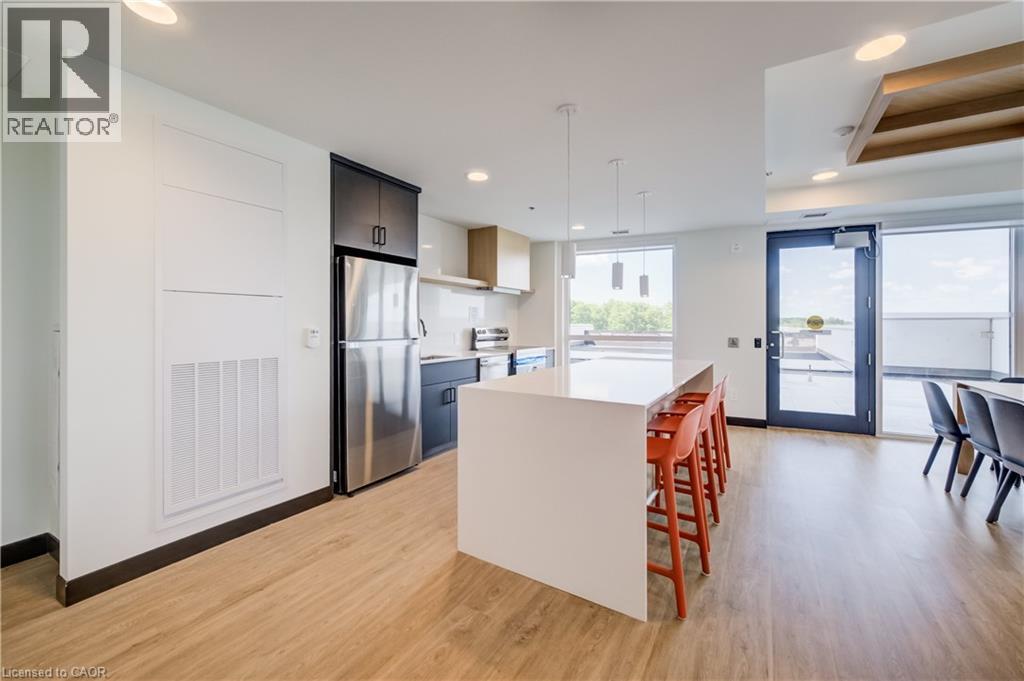 Open-concept kitchen and dining area featuring light wood-finish flooring, a contemporary white island with pendant lighting, stainless steel appliances, dark cabinetry, and access to an exterior pati - 1333 Weber Street E Unit# 708, Kitchener, ON - Indoor Photo Showing Kitchen With Upgraded Kitchen