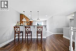 Kitchen bar featuring three pendant lights, a stone-finish countertop, and wood cabinetry with glass-front accents - 