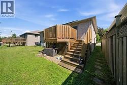 Rear exterior featuring a raised wooden deck with full balustrade and stairs, light brick siding, a natural grass lawn, and a wooden privacy fence - 