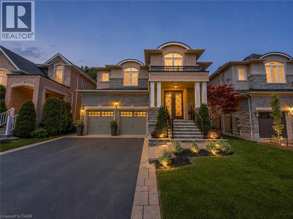 Striking contemporary residence showcasing a symmetrical stone and brick facade with dual three-car garage doors, arched architectural detailing, and illuminated entry portico - 80 Sutherland Crescent, Ancaster, ON - Outdoor With Facade