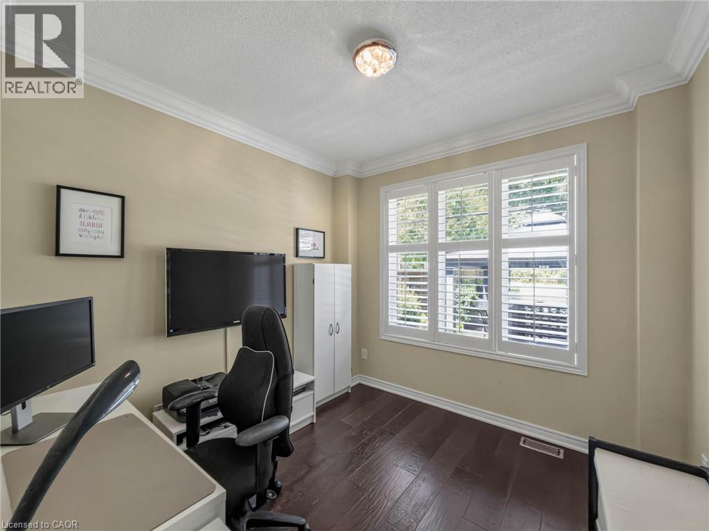Dedicated home office featuring dual monitor setup with dark wood-finish flooring, soft yellow wall finishes, and abundant natural light from multi-pane windows with plantation shutters - 80 Sutherland Crescent, Ancaster, ON - Indoor Photo Showing Office