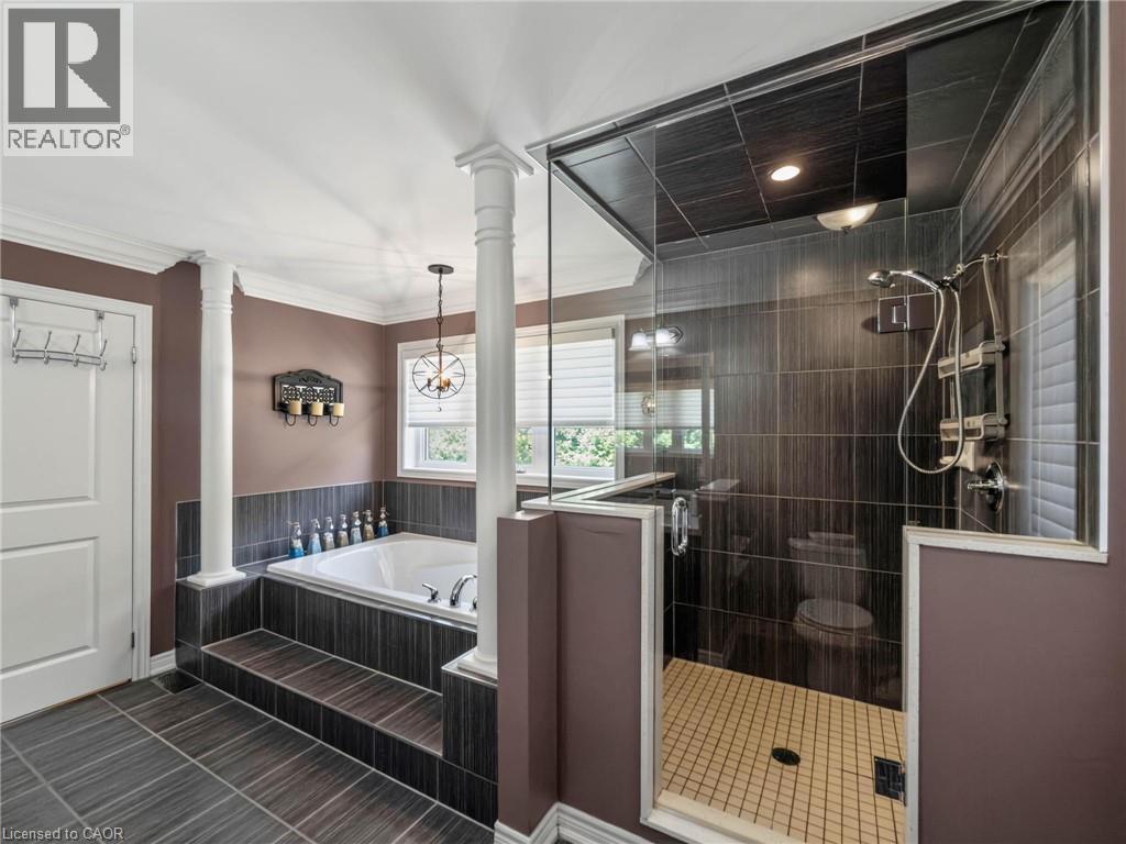 Spa-inspired primary bathroom featuring a freestanding soaking tub with black tile surround, frameless glass shower enclosure with rainfall showerhead, dual vanity with vessel sinks, heated towel rack - 80 Sutherland Crescent, Ancaster, ON - Indoor Photo Showing Bathroom