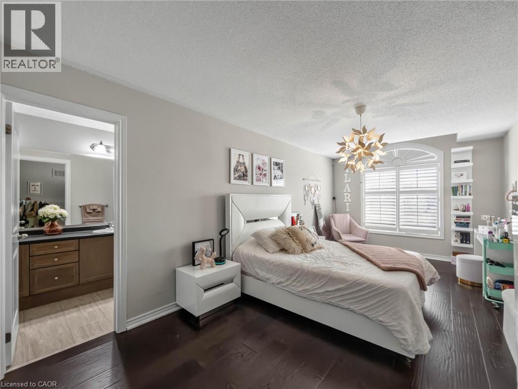 Spacious room featuring dark wood-finish flooring, a decorative ceiling light fixture, and a large window with white plantation shutters - 80 Sutherland Crescent, Ancaster, ON - Indoor Photo Showing Bedroom