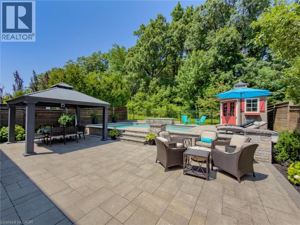 Expansive paver patio featuring a built-in pool and spa, covered gazebo, and a detached shed - 80 Sutherland Crescent, Ancaster, ON - Outdoor With In Ground Pool With Deck Patio Veranda