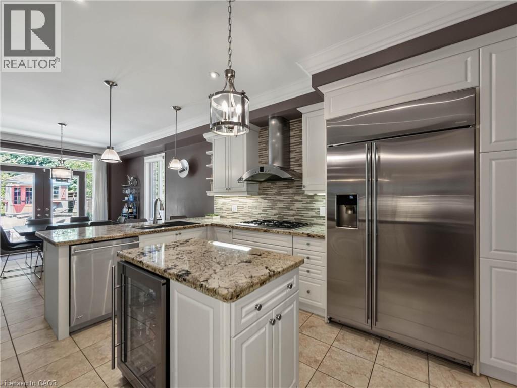 Kitchen featuring a large stainless steel refrigerator, white cabinetry, granite countertops, tile backsplash, and a central island with a built-in wine refrigerator - 80 Sutherland Crescent, Ancaster, ON - Indoor Photo Showing Kitchen With Upgraded Kitchen