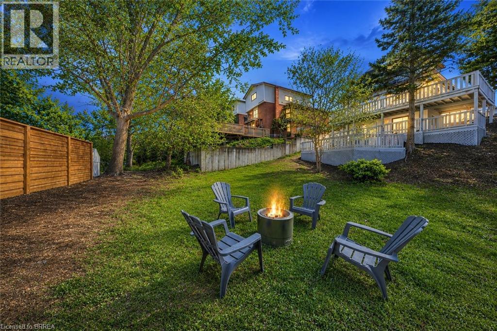 Expansive backyard oasis featuring a manicured lawn, mature landscaping with established trees, a built-in fire pit seating area with Adirondack chairs, and professional hardscaping - 23 Aberdeen Street, Caledonia, ON - Outdoor