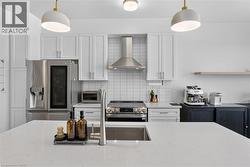 Modern kitchen featuring white shaker cabinetry, stainless steel French-door refrigerator, and gas range with stainless steel hood - 