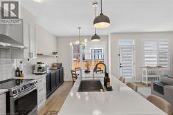 Modern kitchen featuring a white shaker-style cabinetry suite, stainless steel gas range with hood, quartz waterfall-edge island with undermount sink, pendant lighting, wood-finish flooring, and abund - 