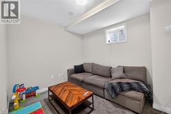 Finished Basement Recreation Room featuring a gray upholstered sectional sofa, wood-finish herringbone coffee table, neutral carpeting, and a small high window - 