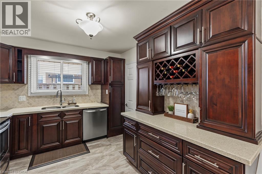 Kitchen featuring rich wood cabinetry, light-toned countertops, a stainless steel dishwasher, and a built-in wine rack with stemware storage - 167 Berkindale Drive, Hamilton, ON - Indoor Photo Showing Kitchen With Double Sink