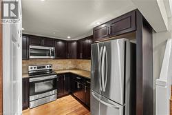Kitchen featuring stainless steel appliances, dark wood cabinetry, natural stone backsplash, and recessed lighting -