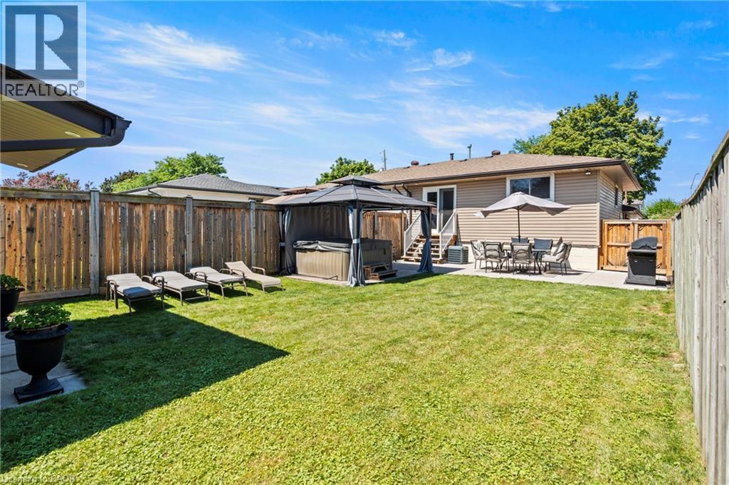 Expansive backyard featuring a manicured lawn, full privacy fencing, a concrete patio with umbrella, and a built-in spa under a gazebo - 167 Berkindale Drive, Hamilton, ON - Outdoor