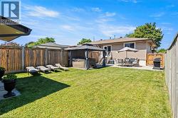 Expansive backyard featuring a manicured lawn, full privacy fencing, a concrete patio with umbrella, and a built-in spa under a gazebo -