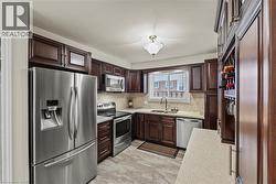 Kitchen featuring rich wood cabinetry, stainless steel appliances, light-toned countertops, and a tile backsplash -