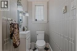 Compact powder room featuring white subway tile wainscoting with geometric panel detailing, a streamlined pedestal sink with chrome fixtures, and a low-profile toilet - 