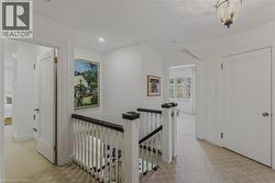 Bright upper-level hallway featuring white painted walls, wood-finish flooring, and a classic staircase with white balusters and black handrail - 