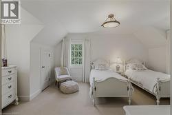 Bright, light-filled bedroom suite featuring dual twin beds with turned-post frames, sloped ceilings with recessed lighting, neutral carpet flooring, and a wall of windows with traditional muntins and - 