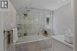 Spa-inspired primary bathroom featuring marble-look tile walls and flooring, a frameless glass-enclosed soaking tub with integrated shower, polished chrome fixtures, recessed lighting, and a built-in - 