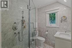 Spa-inspired primary bathroom showcasing marble-look tile walls, a frameless glass-enclosed shower with dual showerheads and hand-held spray, a white floating vanity with integrated sink, chrome fixtu - 