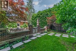 Professionally landscaped backyard featuring a manicured lawn, mature shade trees with rich seasonal foliage, and a custom hardscape pathway of large-format pavers - 