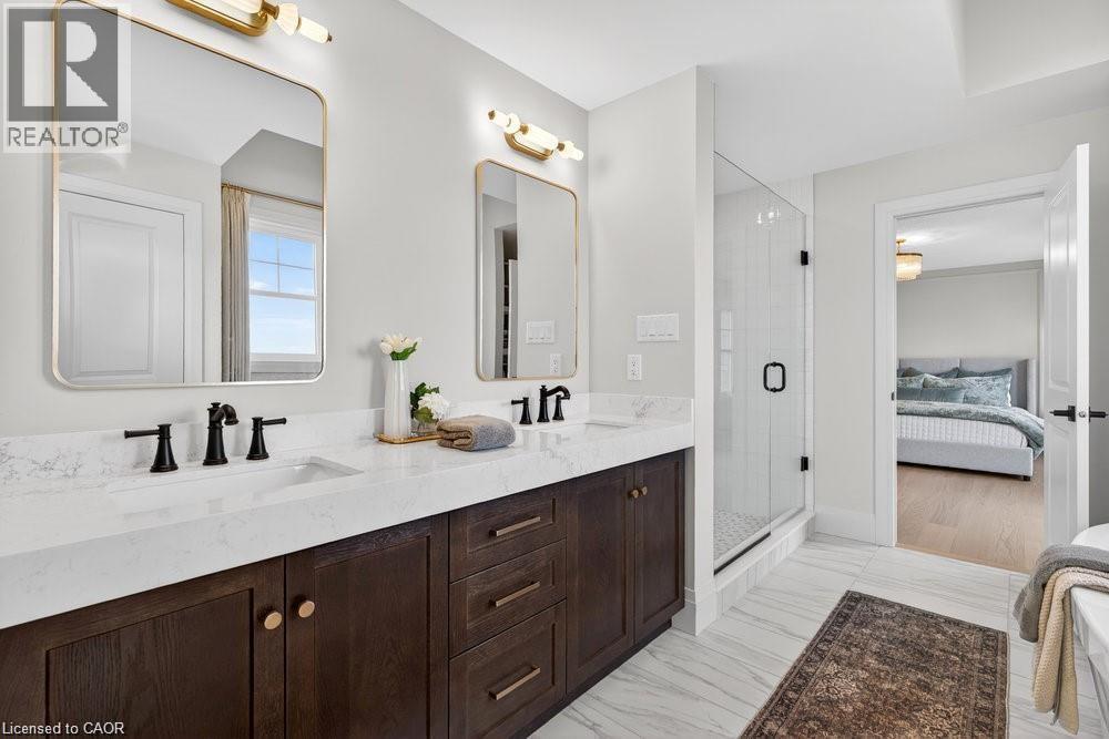 Spa-inspired primary bathroom featuring a dark wood double-vanity with brass hardware, marble countertops, and dual brass-framed mirrors with integrated lighting - 100 Watershore Drive Unit# 15, Hamilton, ON - Indoor Photo Showing Bathroom